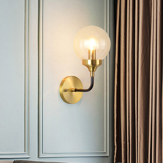 Simple Globe Wall Lighting Clear Glass 1 Bulb Sconce Light Fixture in Brass with Curved Arm Brass Clearhalo 'Cast Iron' 'Glass' 'Industrial' 'Modern wall lights' 'Modern' 'Tiffany' 'Traditional wall lights' 'Wall Lamps & Sconces' 'Wall Lights' Lighting' 331356